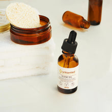 Load image into Gallery viewer, Natural Vegan Glow Oil - Open 30 mLbottle with naturall loofah in the background and empty glow oil bottles