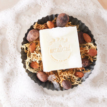 Load image into Gallery viewer, UnscentedSeamossSoapBar_SoapBarBrandedwithUntaintedLogosittingontopofrawseamoss_almonds_cocoainsideofaemptyreesespiecescup